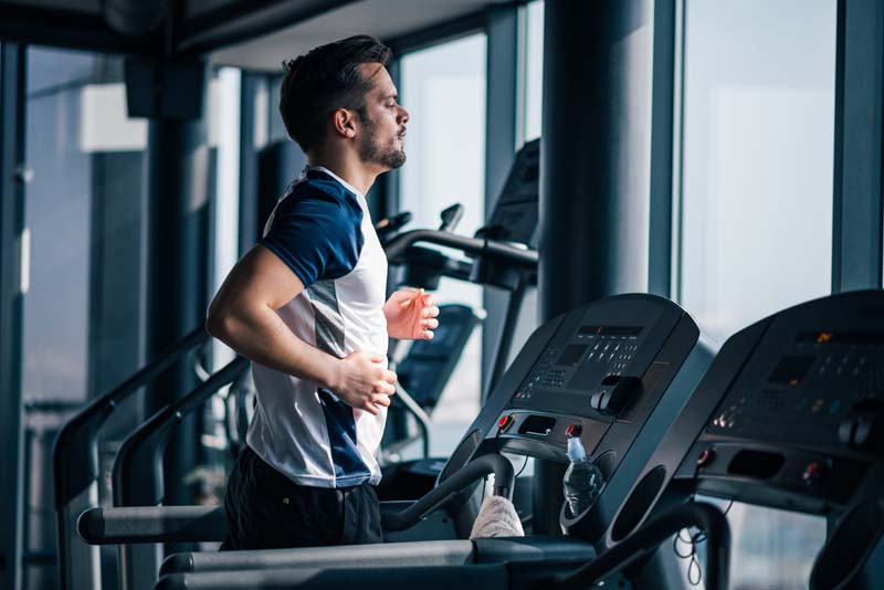 Athletic Man Running On Treadmill , Looking At Window. Athletic Man Running On Treadmill , Looking At Window.